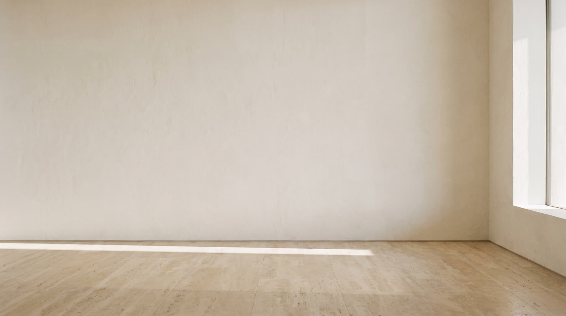 Mur de plâtre crème et sol de travertin dans une pièce vide, traversés par la lumière du matin